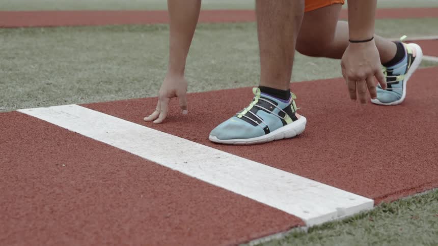 Man crouches in front of a white line on a track then begins to run