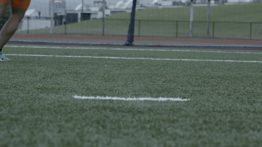 A man is kicking a soccer ball on a field in daylight