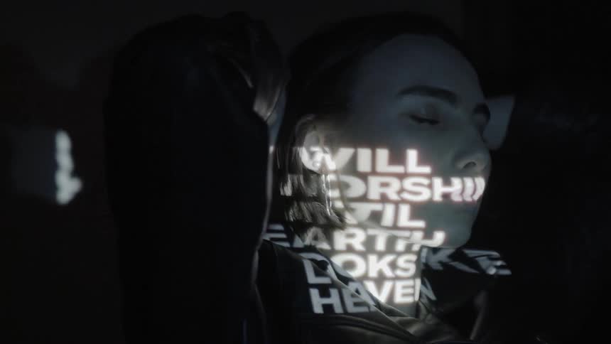Words are being projected on a woman standing in a dark room