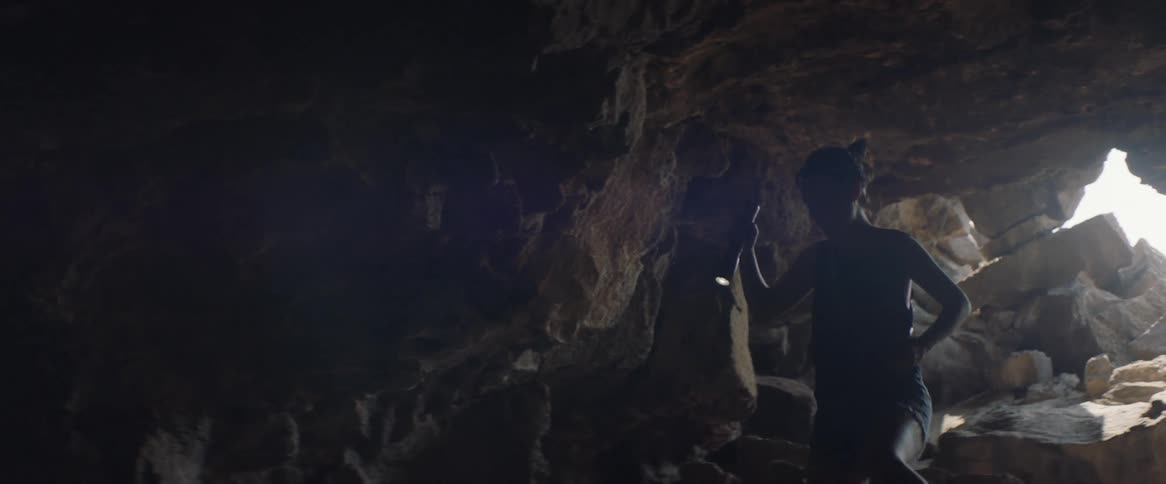 A woman carries a flashlight in a dark cave