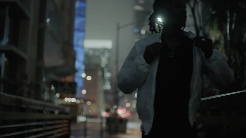 A man adjusts his jacket while walking in a city at night