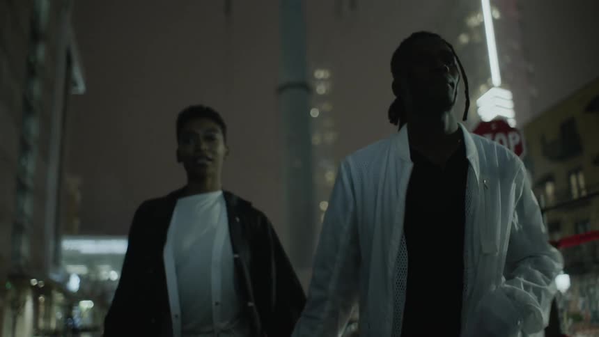 A couple holds hands while walking in the city at night