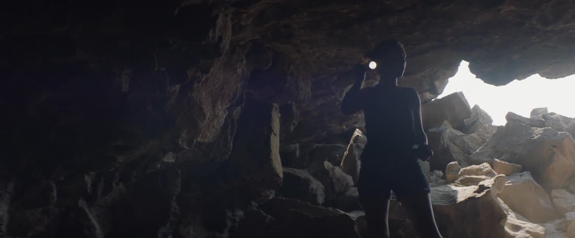 Woman shines her flashlight as she enters a dark cave