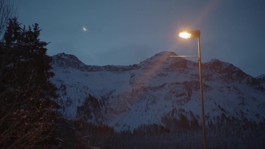Snowy mountains in the dawn, street lamp in the foreground