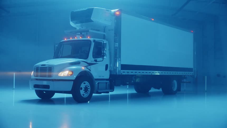 A large truck is parked in a warehouse with flashing lights