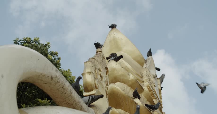 Pigeons land on a gold statue on a sunny day
