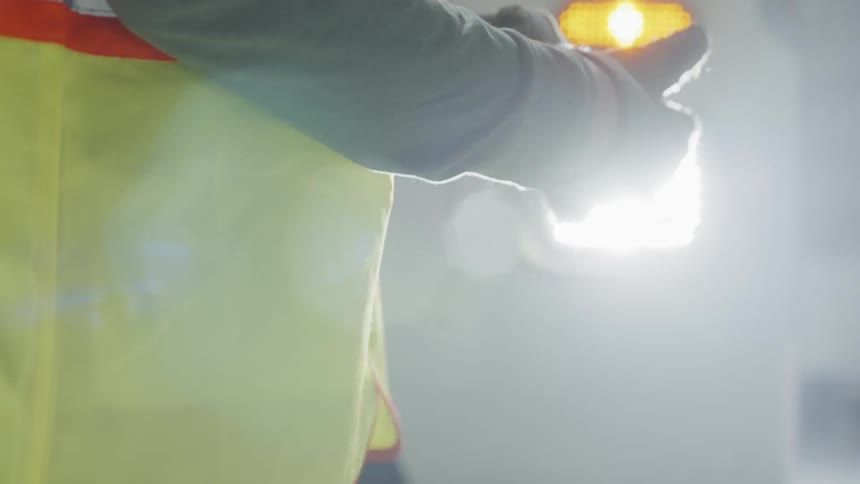 A worker puts  on gloves in the glare of headlights