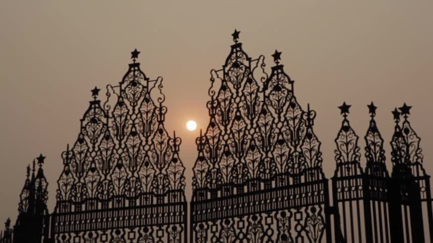 The sun shines between cast iron fence