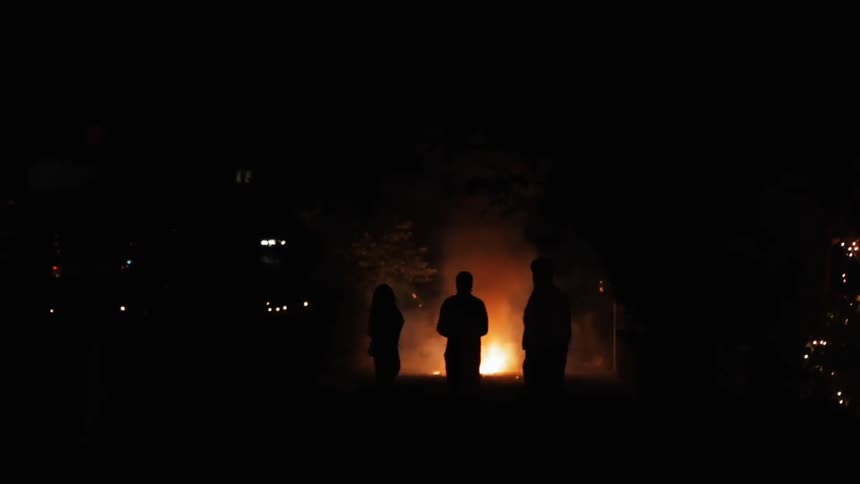 Three people standing in front of a blazing fire at night
