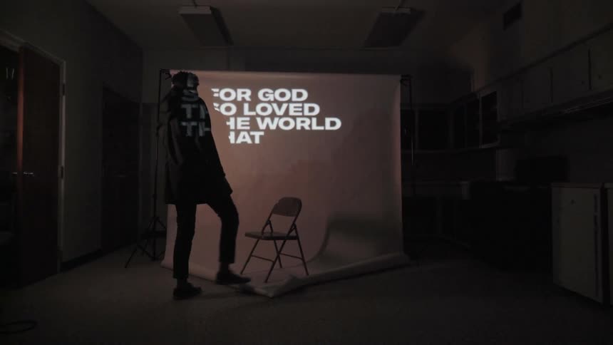 A man walks towards a chair as words are projected