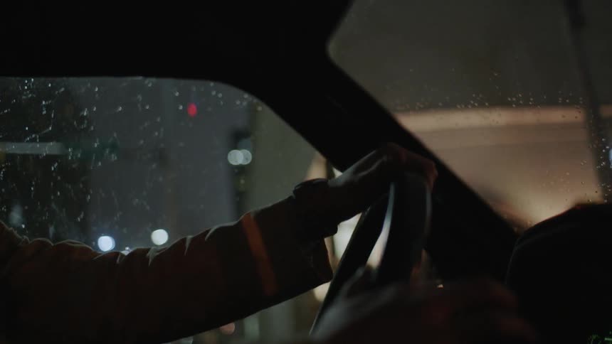 A man is driving a van through a city on a rainy night