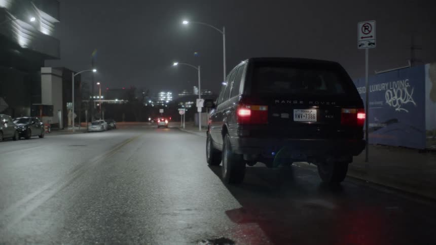 A range rover is driving off down an urban street at night