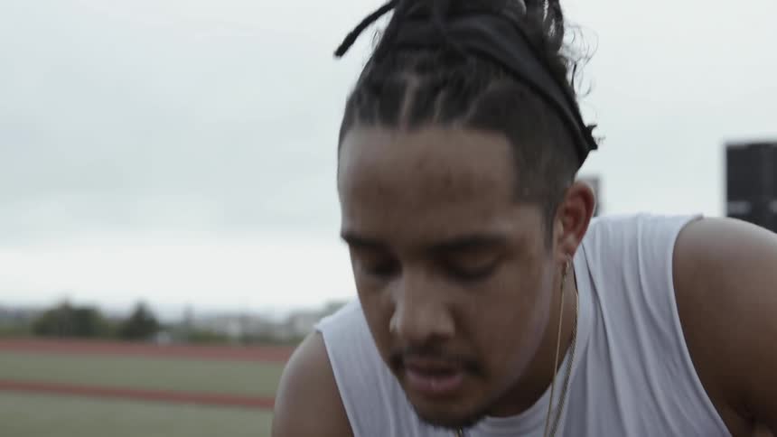 An athlete is breathing heavy as he rises from kneeling on an athletic field in daylight