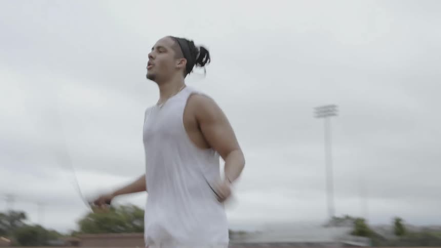 A male athlete is jumping rope outside in a sports complex on a cloudy day