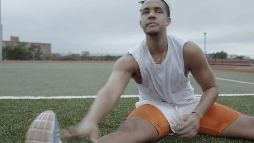 A male athlete is stretching out on an athletic field in daylight