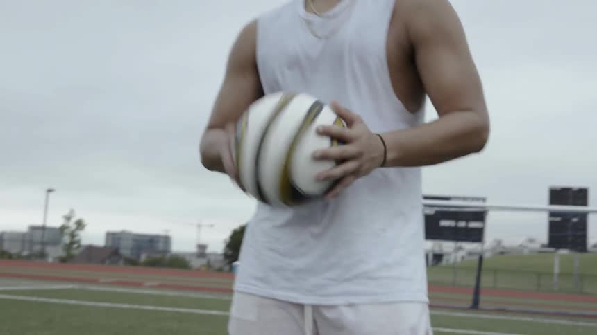 An athlete holds a soccer ball on an outdoor field