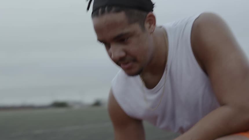 A male athlete is shaking his head and looking around as he kneels on a track on a cloudy day