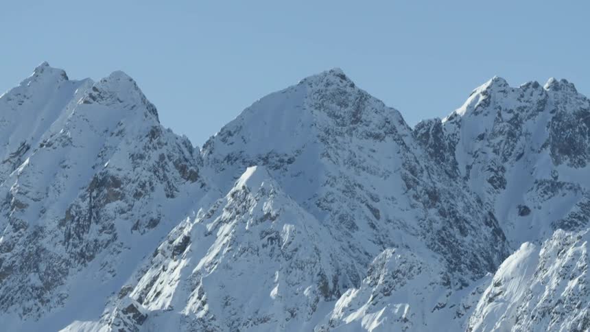 Snow is covering the peaks of a mountain range during the day