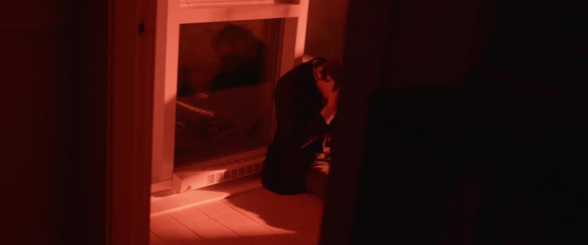 A man is sitting on a floor inside a house and clutching his head