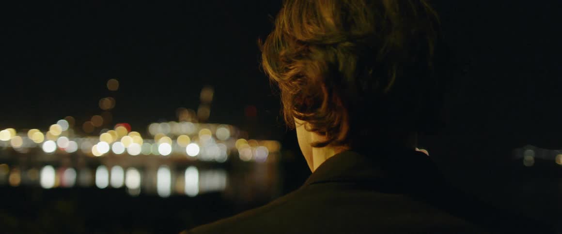A man stands by the water at night