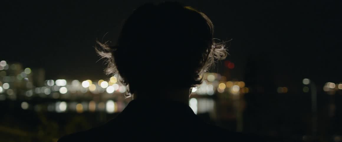 A man looks out towards the city lights at night