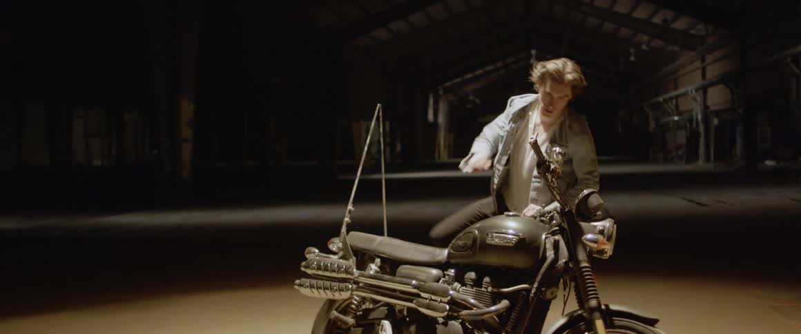 A man puts his jacket on and mounts a motorcycle at night