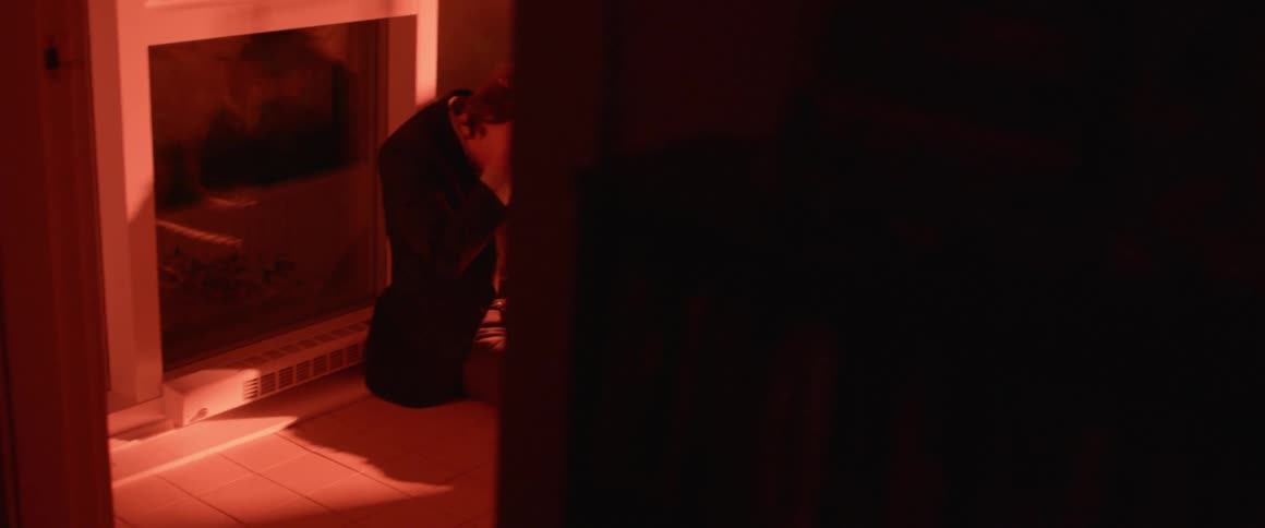A man sits worrying on the floor of a dark room with flashing red lights
