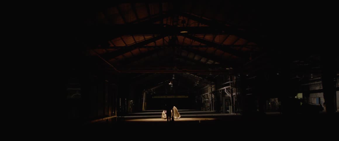A man walks towards a motorcycle in a dark warehouse