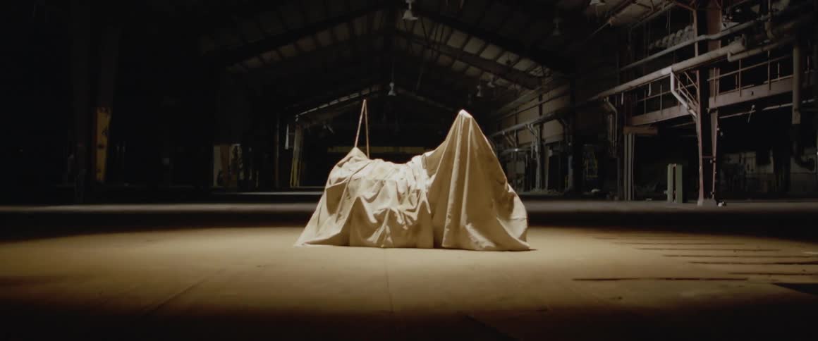 A cloth covers a motorcycle in a warehouse