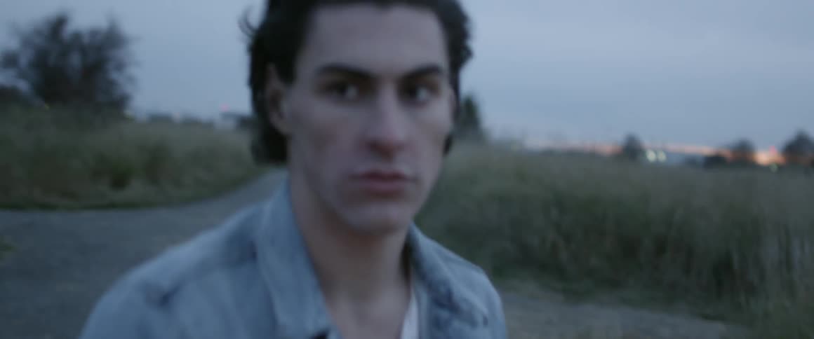 Man gets off of a motorcycle while in a field