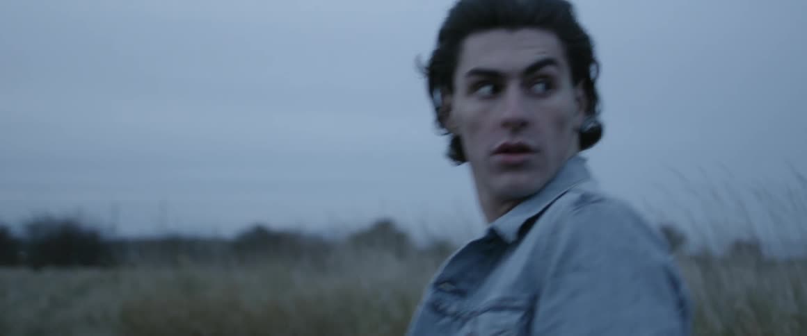 A man in a denim jacket walks in a rural field