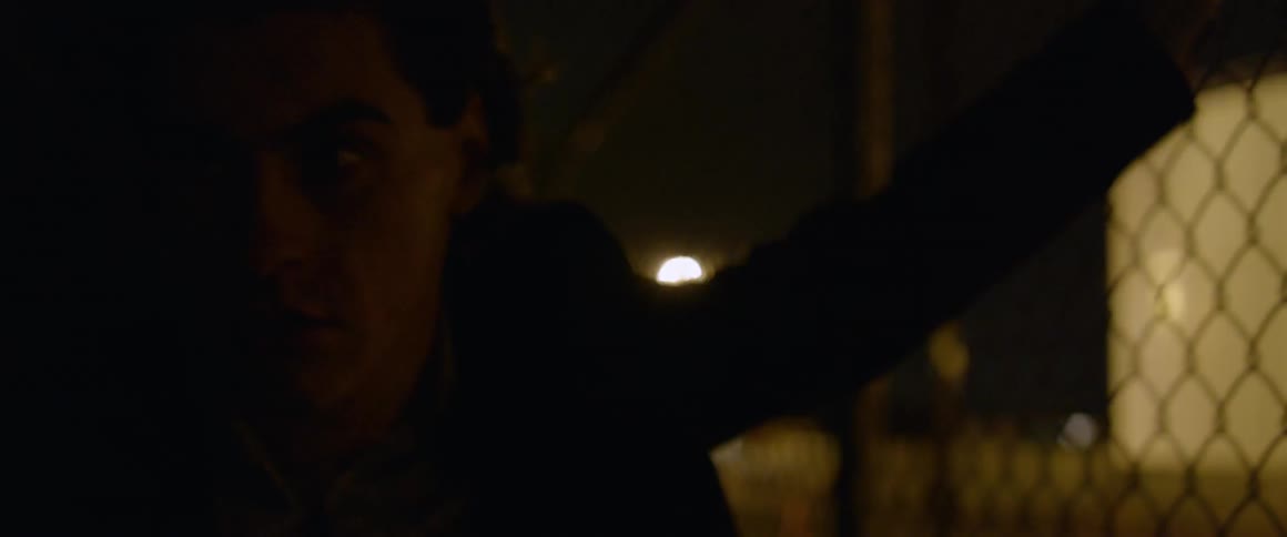 Man looks through a chain link fence at night