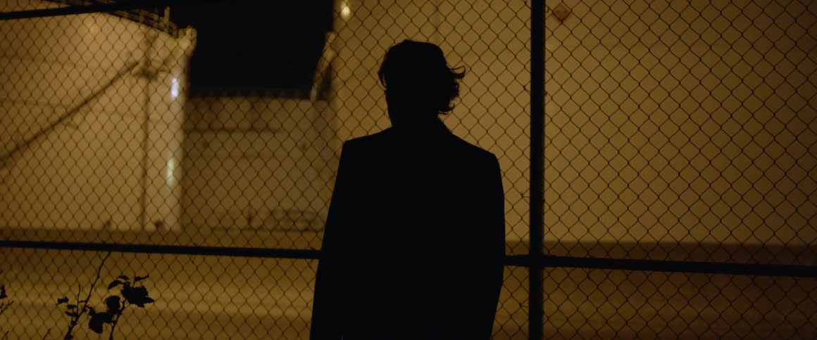 A man stands by the tall fence