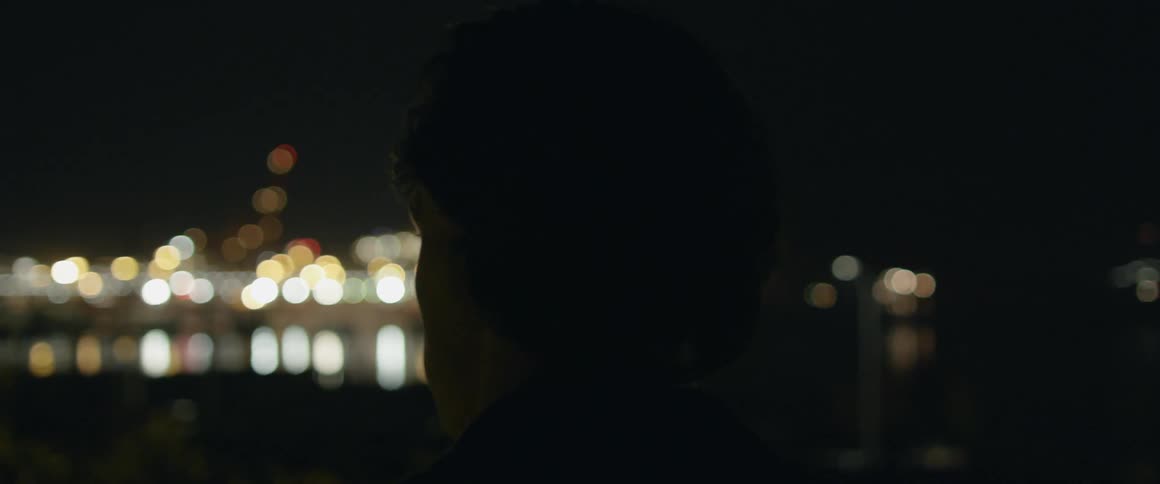A man stands by the water at night