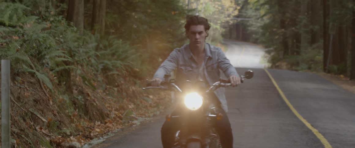 A man rides a motorcycle down the woodsy road