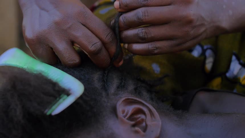 Closeup on the hands of an black woman braiding a young girl's hair