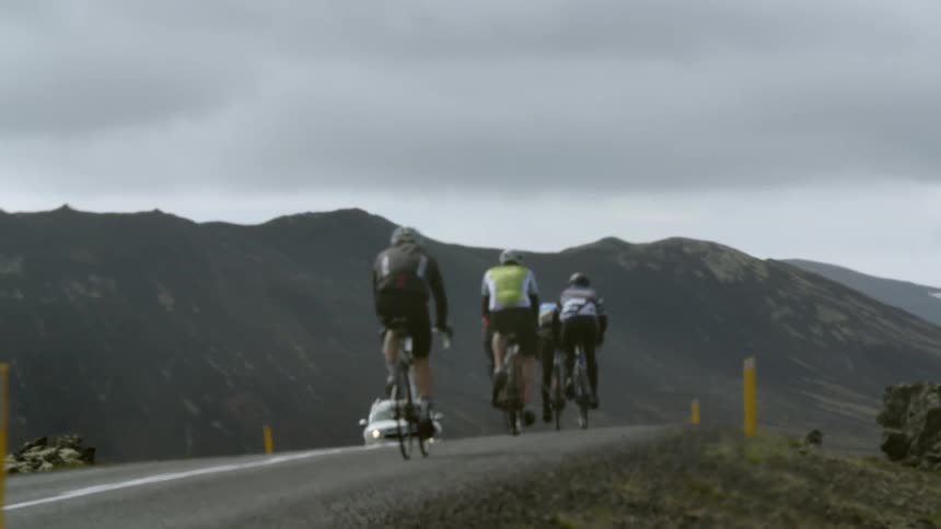 Cyclists bike towards a mountain on an overcast day