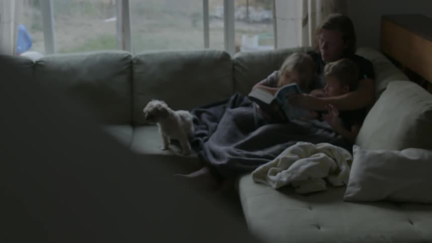Adult reading to two children and a small dog on a couch
