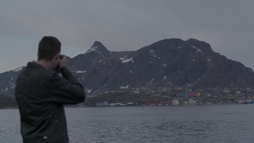 Man taking pictures of a mountain across a lake