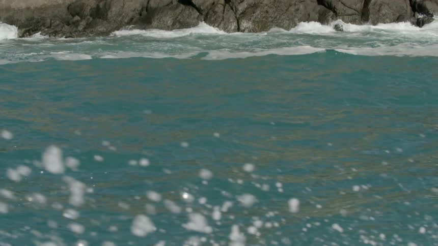 Shoreline rocks seen from a boat traveling in a river while water foams and splashes around