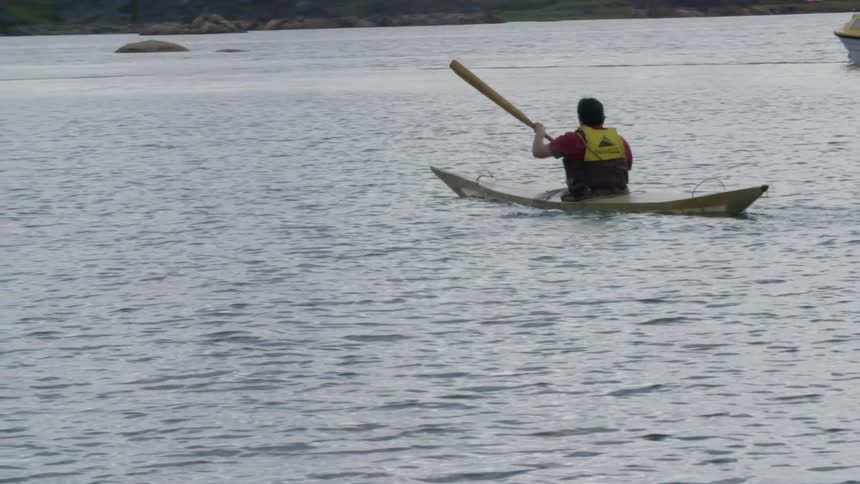 A man wearing a safety vest paddles a canoe on a lake