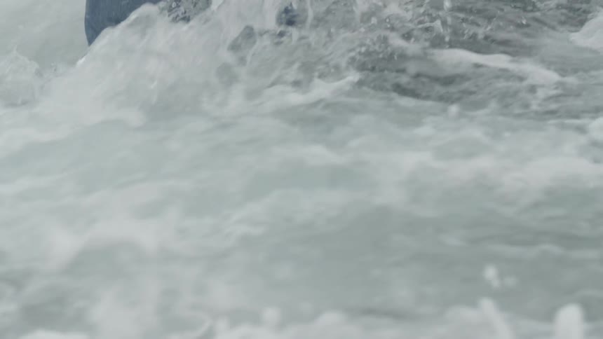 Person standing knee-deep in water as it crashes on his legs