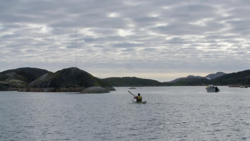 A kayaker paddles on a lake and a boat floats nearby