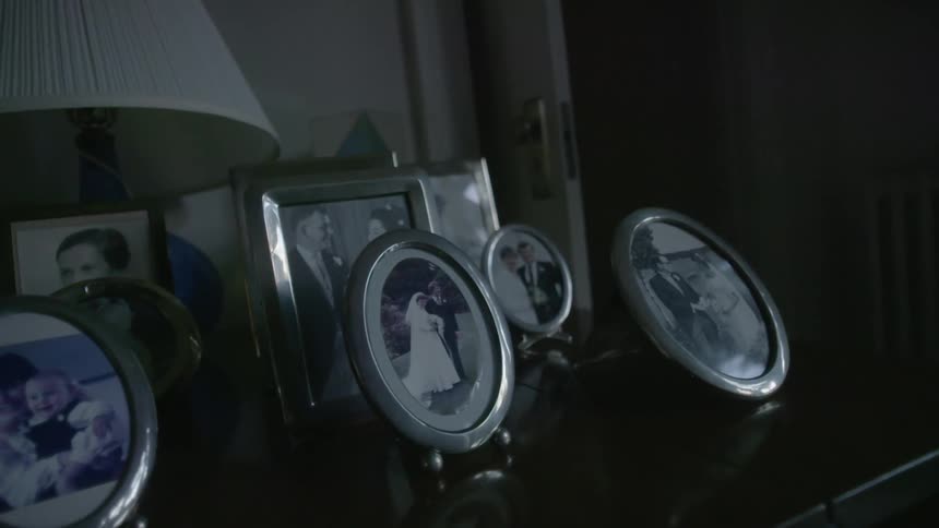 Many framed pictures on a table in front of a lamp