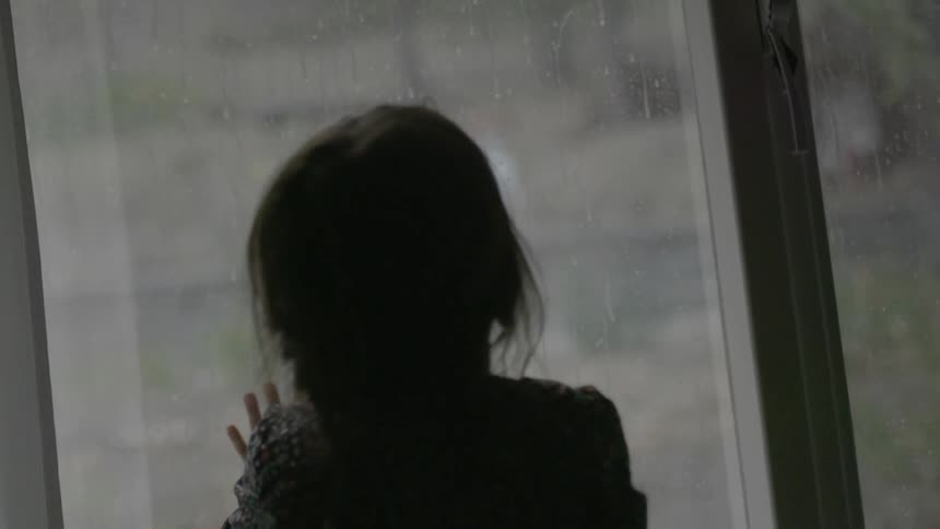 A girls looks out a window at the rain