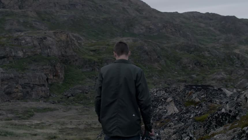 A man walks on a mountainside on an overcast day
