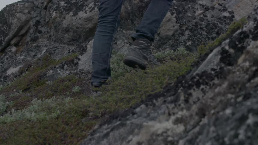A man with a camera climbs up a rocky hill