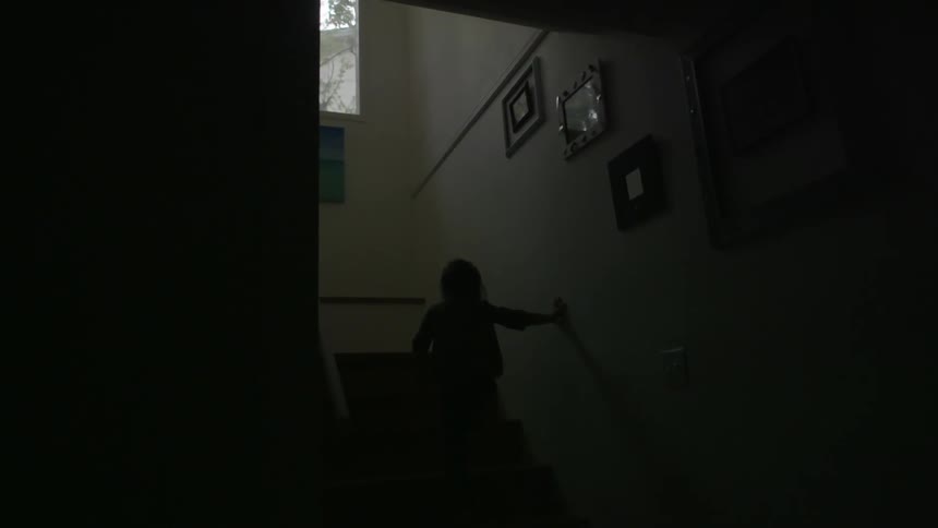 A very young girl runs up some stairs in a darkened home