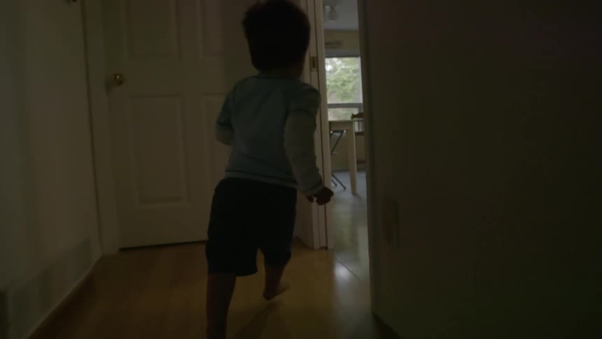 A toddler runs down a hallway and into a kitchen