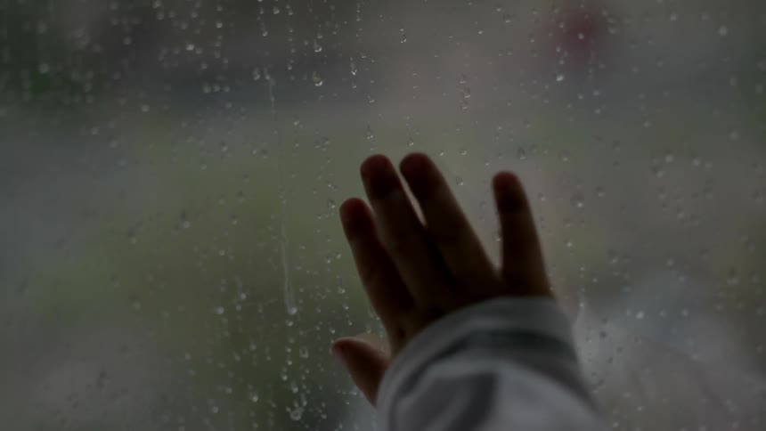 Young child watching the rain outside from behind glass